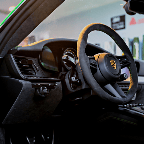 Smul luxury car freshener attached to the car's air inlet to the left of the steering wheel. View is looking from the drivers open door. The car is a Porsche 718 Cayman GT4